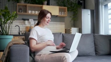 Pregnant woman wife communicates with husband, parents, grandparents, friends via video call remotely. He talks online via webcam using laptop computer while sitting at home in living room on the sofa