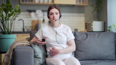 Portrait young pregnant business woman works remotely make a meeting, conference, briefing or interview online by video call looking at camera. Female freelancer at home during pregnancy webcam view