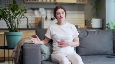 Portrait Young pregnant woman patient consults online with doctor on video call listens to advice appointment looking at camera sitting at home on sofa. Remote meeting consultation. View webcam screen