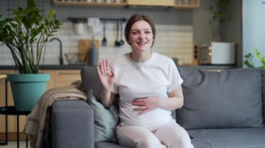 Pregnant woman wife communicates with parents, grandparents, friends via video call remotely. talks online via webcam view using laptop computer sitting at home in living room on sofa look at camera