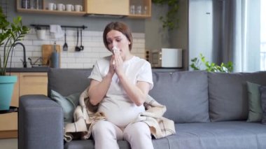 sick pregnant woman with cold cough and temperature blowing nose with runny nose sitting on sofa at home. ailing female got flu during pregnancy. Disease. suffering Allergy cold symptoms