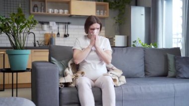 sick pregnant woman with cold cough and temperature blowing nose with runny nose sitting on sofa at home. ailing female got flu during pregnancy. Disease. suffering Allergy cold symptoms