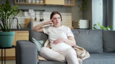 pregnant woman, feeling unwell. suffering morning sick home headache, depression during pregnancy sitting on the sofa in the living room. Indoor. unhealthy Female worries, anxiety