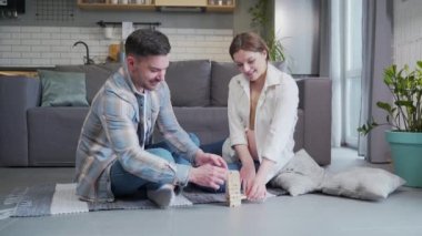 Young family. Pregnant woman and man sitting on the floor at home playing board game. Make a tower of wooden bars. Have fun happy couple spend leisure time together during pregnancy. indoor
