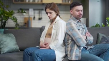 Family conflict. Young couple, pregnant woman and man sitting on sofa at home with their backs to each other. Do not talk, offended. spouses after a quarrel with a bad mood and misunderstanding