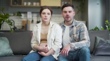 young family listens online consultation during pregnancy. Pregnant woman and man talking look at camera and receive advice from a doctor remotely. View webcam. Preparation for childbirth at home