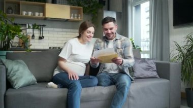 couple opening envelope with letter and happy for good news, positive confirmation. Sitting at home. Joyful Family unfolding document receives a notification read bank notice rejoice feel happiness
