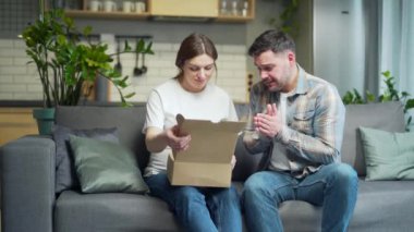 shocked frustrated couple customer open cardboard box receive wrong or damaged shopping order parcel. Sad young man and pregnant woman unpacking parcel, delivery mistake Upset mad unhappy people