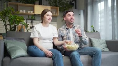 Excited young couple, pregnant woman and man cheering for match or team watching TV sports competition at home on couch. spend leisure time during pregnancy together. happy fans rejoices shout exclaim