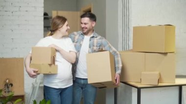 a young pregnant couple with boxes moves into a new apartment. home holding cardboard box. Family expecting baby. House mortgage