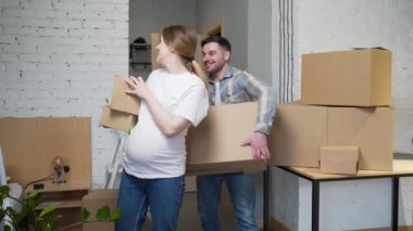 a young pregnant couple with boxes moves into a new apartment. home holding cardboard box. Family expecting baby. House mortgage