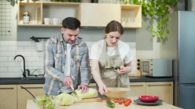 Cheerful happy family couple expecting a baby spend a funny time together in the kitchen at home. A pregnant woman and her husband are dancing and having fun while cooking prepare lunch singing