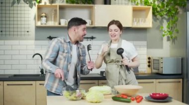Cheerful happy family couple expecting a baby spend a funny time together in the kitchen at home. A pregnant woman and her husband are dancing and having fun while cooking prepare lunch singing
