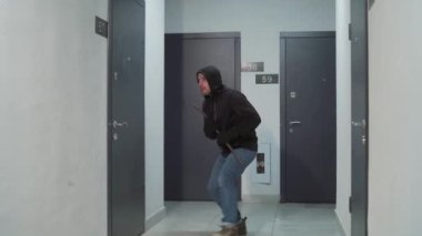 burglar or thief breaks down a door in a house or apartment and enters. Surveillance camera type. An attacker or thug cracking the door of the flat. Masked Bandit using lock picker