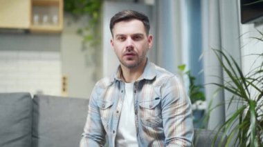 Young handsome man in casual clothes listens to a conference meeting, consultation or advice online while looking at camera. Male in the home by video call remotely in the room. Webcam view portrait