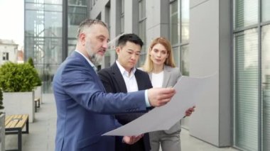 Diverse group business people outside office building, talking discussing new construction plan, team engineers and designers discuss holding and looking Technical drawing, drafting project