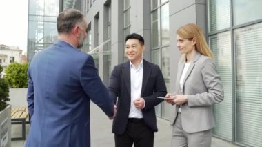 meeting of business team partners outside. Negotiations of a group of business people shaking hands, getting to know each other, discussing a project near an office building diverse employees in suit