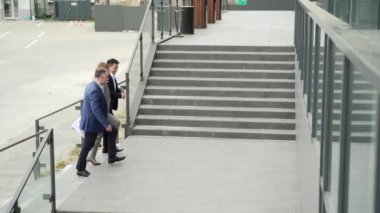 A group of business people climb up the stairs to an office building. rear back view A team of partners are walking down the street of downtown. outside. Colleagues employees go. Mature Man and woman
