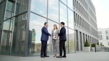 International business team meeting. mature man, Caucasian woman, Asian employee communicate . group of entrepreneurs in formal suits discuss a project document near office center on street. Outside