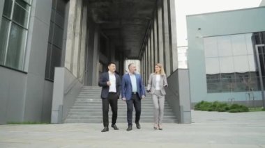 business people, colleagues, employees go along the street near the building office center. A team of partners communicate while walking outside. diverse group of entrepreneurs discuss the project