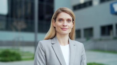 close-up portrait attractive happy business woman employee looking at camera smiling. Face Caucasian female blonde middle-aged worker standing on a city street near urban office center outside outdoor