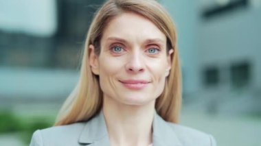 close-up portrait attractive happy business woman employee looking at camera smiling. Face Caucasian female blonde middle-aged worker standing on a city street near urban office center outside outdoor