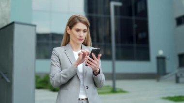 business woman employee entrepreneur looking phone smartphone with shouts win gesture, read good news, investment, profit growth. Happy female investor rejoices celebrate victory won outside office