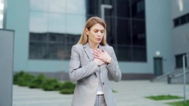 Young female employee feels a strong Sudden pain in the heart while standing on the street. Female Holding chest having heartache symptom heart attack. Overworked woman outdoors