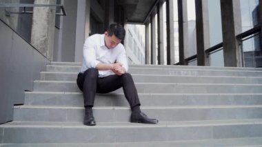 sad asian business man employee with depression worker sitting on stairs on city street near office building. outside. jobless fired businessman Lay off. Dissmissal manager Disappointed crisis problem