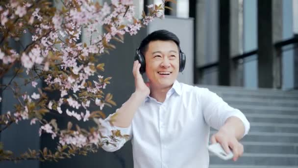 Cheerful Asian Man Headphones Listening Music Dancing Smartphone Hands Standing — ストック動画