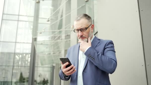 Serious Thoughtful Business Man Uses Smartphone While Standing Office Building — Stok video