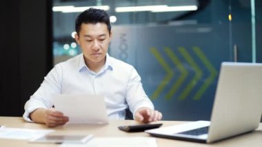 Yoğun çalışan, ofis işyerinde çalışan muhasebeci, kar vergilerini sayan evrak işleri rutin Asyalı erkek girişimci yöneticisi, istatistikleri analiz eden, mali raporlar hazırlayan.