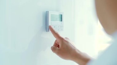 Adamın elini kapatıp düğmelere basıyor daire ve ofis için klima ve ısıtma kontrol paneli beyaz bir duvarda bulunuyor. Kapat.