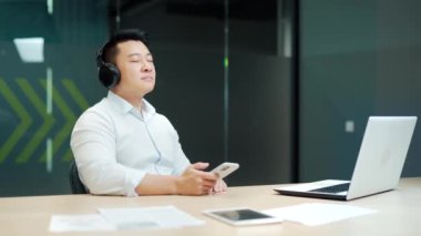 İş adamı dinlenmeyi ve ofiste kulaklıkla dinlenmeyi sever. Bilgisayar masasında dinlen. Mutlu işçiler, işyerindeki işyerindeki işyerinde telefon kullanarak huzur içinde çalışanların keyfini çıkarıyorlar.