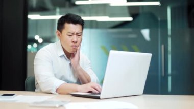 Asian business man employee with severe toothache. male worker manager businessman suffers from Strong pain. Sitting at work in workplace office. painful expression dental illness on teeth indoor Asia