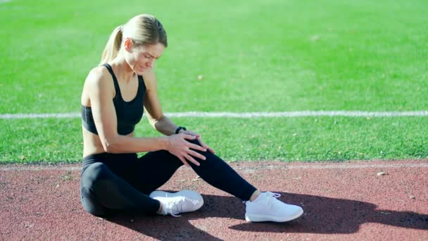 跑步运动员 肌肉酸痛的运动员坐在体育场的跑道上 女子按摩伸展 在室外慢跑时受伤 健康的女性扭伤伸展拉力 腿肌肉痉挛小腿运动 — 图库视频影像