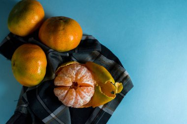 Mavi bir yüzey üzerindeki ekose kumaş parçasında kopyalanmış taze mandalinalar.