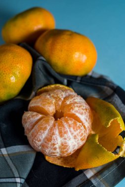 Mavi bir yüzey üzerindeki ekose kumaş parçasında kopyalanmış taze mandalinalar.