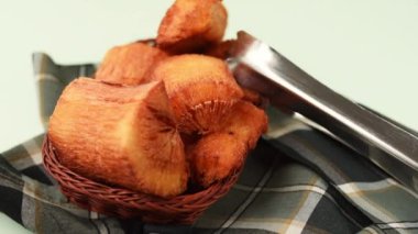 El, yeşil bir yüzey üzerindeki ekose kumaş parçasında bir sepette kızarmış bir yukka alıyor. 