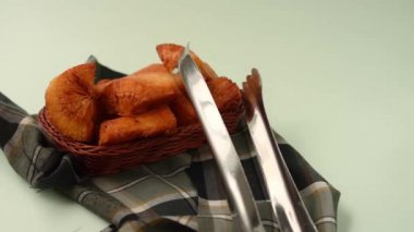 El, yeşil bir yüzey üzerindeki ekose kumaş parçasında bir sepette kızarmış bir yukka alıyor. 