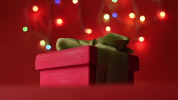 Фокусування Рожевої Подарункової Коробки Зеленою Стрічкою Червоній Поверхні Різдвяними Вогнями — стокове відео