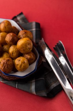 Kızarmış Kolombiya patatesleri kırmızı bir yüzey üzerinde ekose bir kumaş parçasının üzerinde sepetten.  