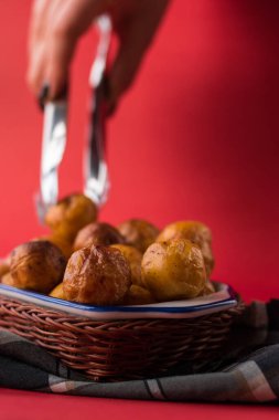 Kırmızı bir yüzey üzerinde ekose bir kumaş parçasının üzerindeki sepetten kızarmış Kolombiya patatesini alan el.  