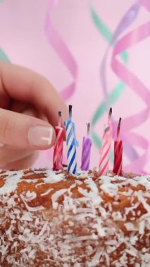Kafkasyalı bir elin pastadan doğum günü mumları alırken çekilmiş dikey videosu ve pembe arka planı olan doğum günü şeyleri. 