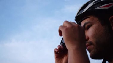 Sakallı adam bisiklet gözlüğü takıyor ve arka planda mavi gökyüzü olan bisiklet kaskı takıyor. 