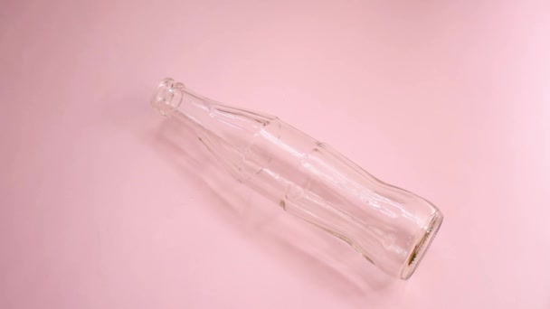 Mano Niña Girando Una Botella Vidrio Sobre Una Superficie Rosa — Vídeo de stock