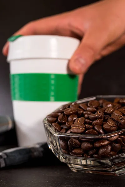 Kahve çekirdekleri ve plastik termos, siyah arka planda bir el tarafından alınan sıcak içecekler için.