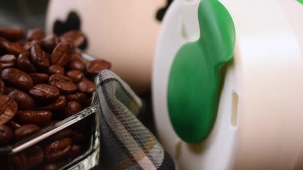 黒の背景に手で取られた熱い飲み物のためのコーヒー豆 ミルクジュグ プラスチック製の魔法瓶のパン — ストック動画