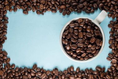 Mavi arka planda geleneksel bir fincanda bir sürü kahve çekirdeği 