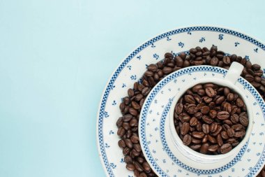 Mavi arka planda geleneksel bir fincanda bir sürü kahve çekirdeği 